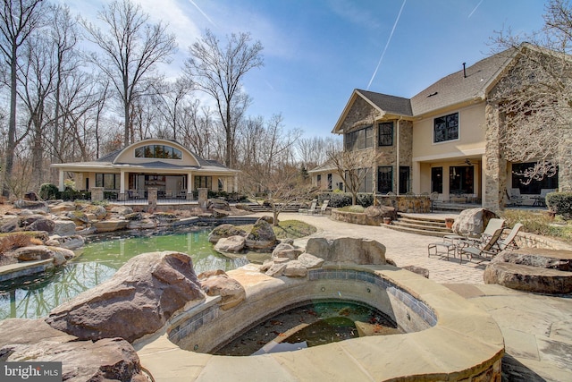 view of swimming pool with a patio, a small pond, and a hot tub