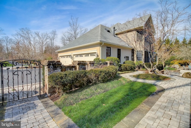 view of home's exterior with roof with shingles, stucco siding, a gate, fence, and a garage