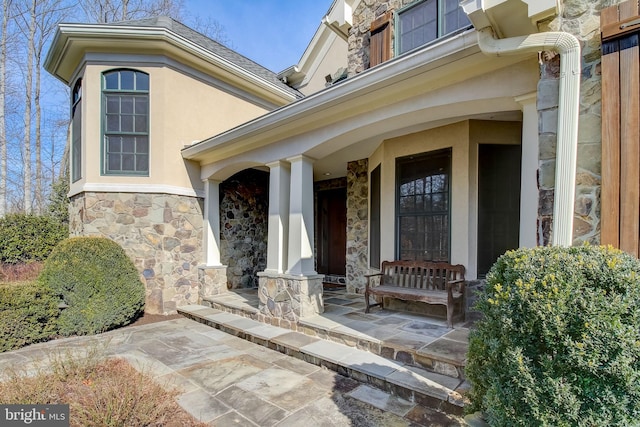 view of exterior entry with stone siding, covered porch, and stucco siding