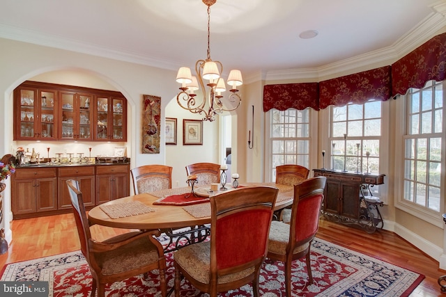 dining area featuring light wood-style floors, baseboards, crown molding, and an inviting chandelier