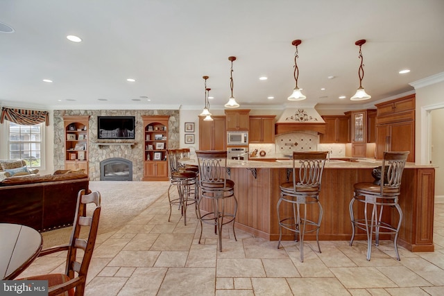 kitchen featuring custom range hood, a breakfast bar area, built in appliances, light countertops, and a stone fireplace