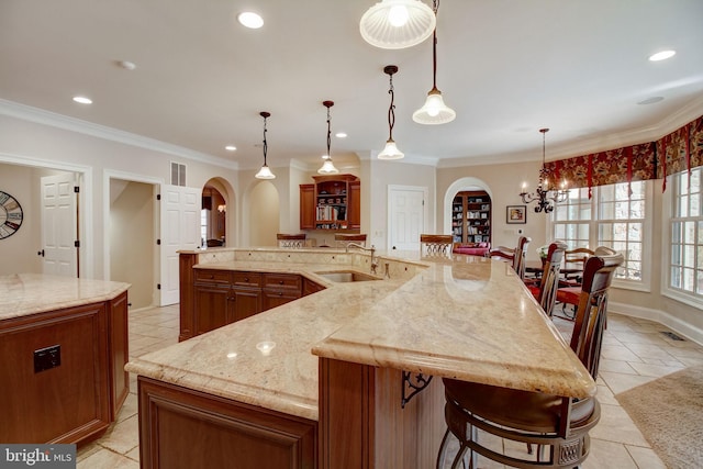 kitchen with arched walkways, crown molding, a large island, a sink, and light stone countertops