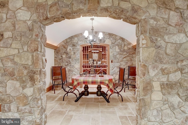 wine cellar with vaulted ceiling, arched walkways, stone tile flooring, and an inviting chandelier