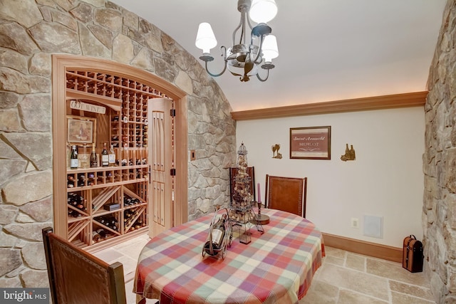 wine room featuring stone tile floors, a chandelier, and baseboards