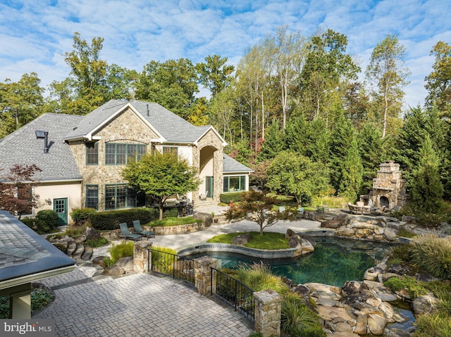 view of front of house featuring stone siding, an outdoor stone fireplace, a patio area, and fence