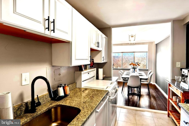 kitchen with light stone counters, range with electric stovetop, white cabinetry, a sink, and light tile patterned flooring