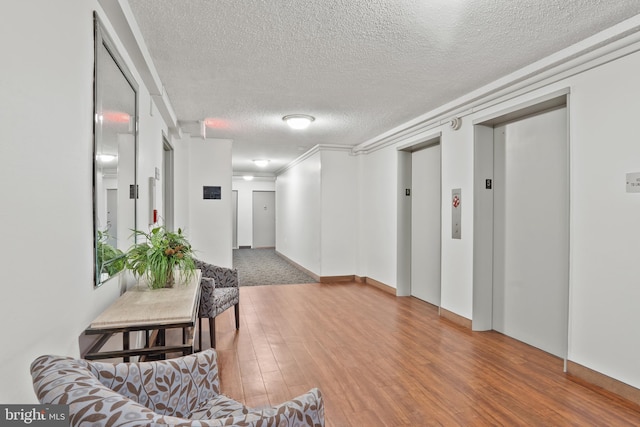 corridor with a textured ceiling, wood finished floors, and elevator