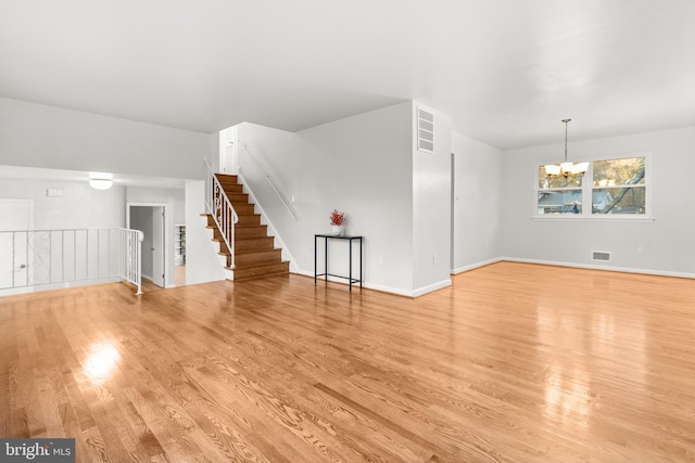 unfurnished living room featuring visible vents, a notable chandelier, stairway, and light wood finished floors