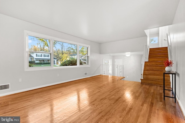 unfurnished living room featuring visible vents, stairway, baseboards, and wood finished floors