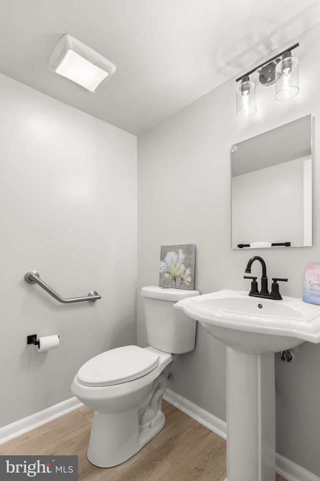 half bathroom featuring toilet, baseboards, and wood finished floors