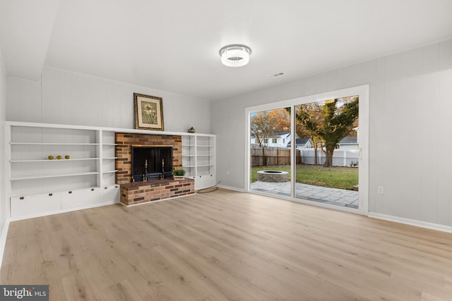 unfurnished living room with a brick fireplace, visible vents, baseboards, and wood finished floors