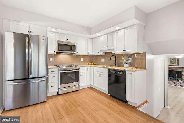 kitchen with appliances with stainless steel finishes, a sink, light wood-style flooring, and white cabinetry