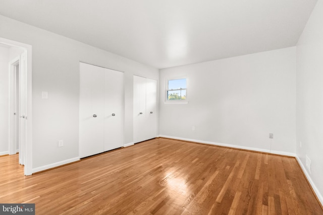 unfurnished bedroom with light wood-style floors, baseboards, and two closets