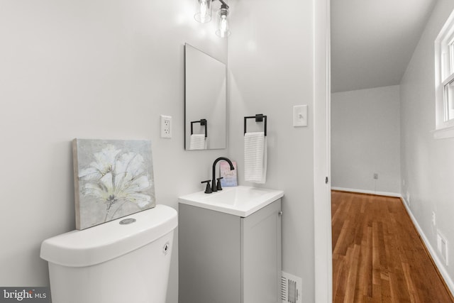 half bath featuring toilet, wood finished floors, vanity, visible vents, and baseboards