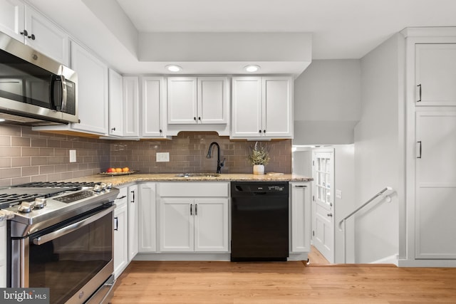 kitchen featuring a sink, white cabinetry, appliances with stainless steel finishes, decorative backsplash, and light wood finished floors