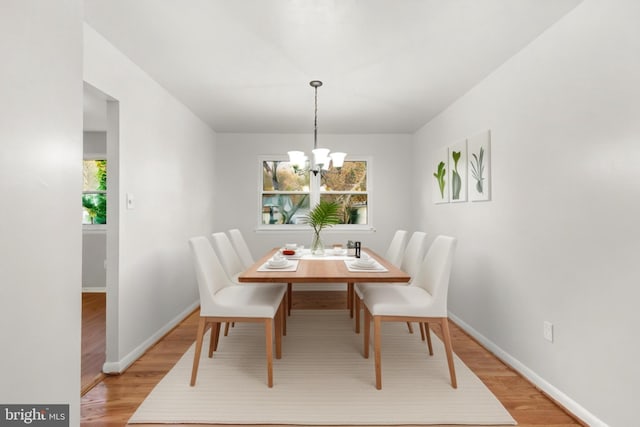 dining area featuring light wood-style flooring, baseboards, and a notable chandelier