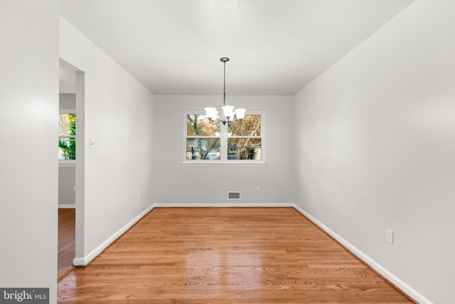 unfurnished dining area with an inviting chandelier, baseboards, visible vents, and wood finished floors