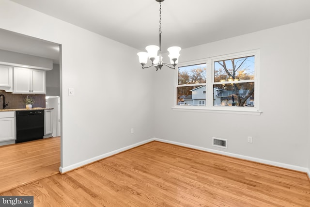 unfurnished dining area with visible vents, baseboards, light wood-style flooring, a chandelier, and a sink