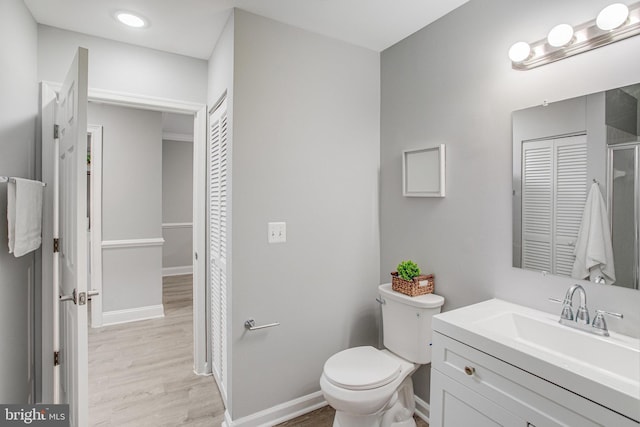 full bathroom featuring toilet, wood finished floors, vanity, baseboards, and a closet