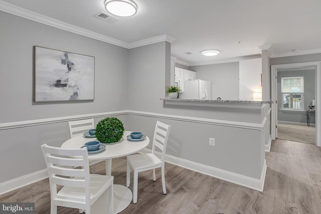 dining space with baseboards, light wood-style flooring, visible vents, and crown molding