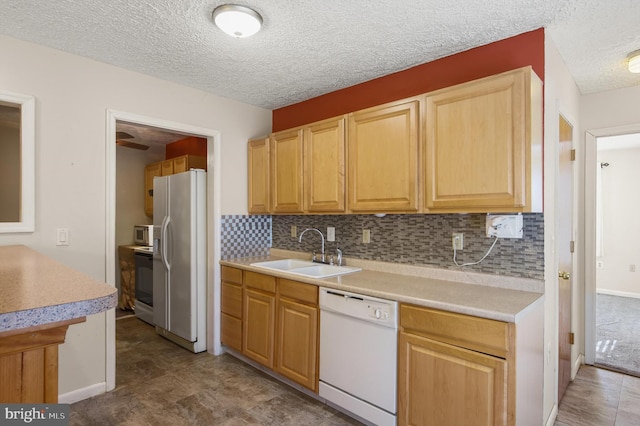 kitchen featuring white appliances, decorative backsplash, light countertops, and a sink