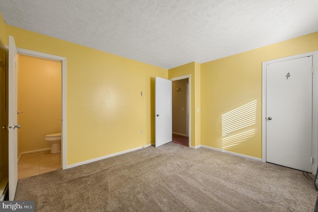 unfurnished bedroom with carpet flooring, a textured ceiling, baseboards, and ensuite bathroom