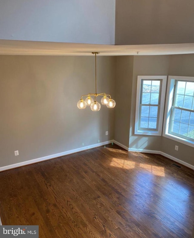 spare room with an inviting chandelier, baseboards, visible vents, and dark wood-type flooring