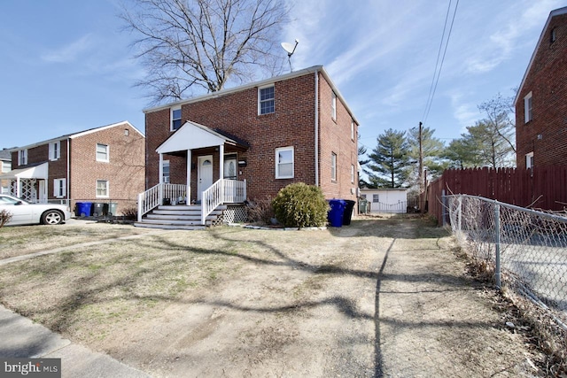 view of front of house with covered porch, brick siding, and fence