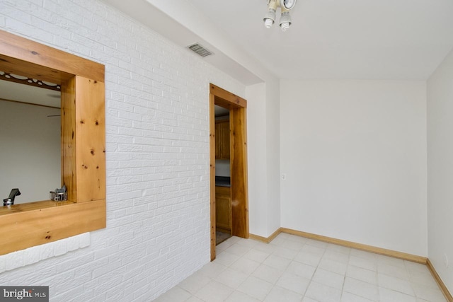 empty room featuring brick wall, visible vents, and baseboards