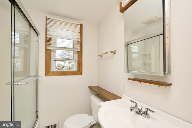 bathroom with toilet, a sink, a shower with door, and visible vents