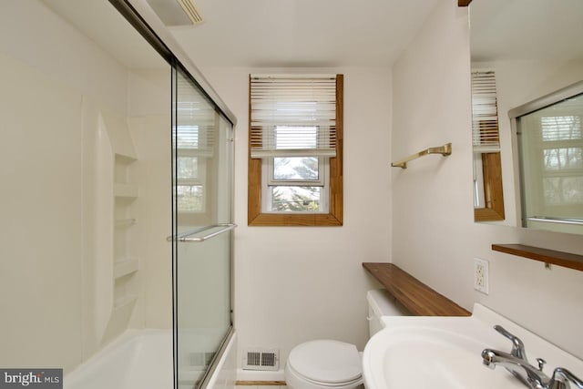 bathroom featuring visible vents, bath / shower combo with glass door, a sink, and toilet