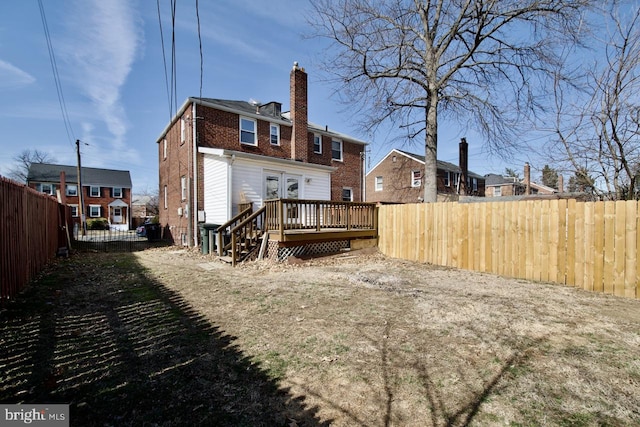 rear view of house featuring a chimney, brick siding, a deck, and a fenced backyard