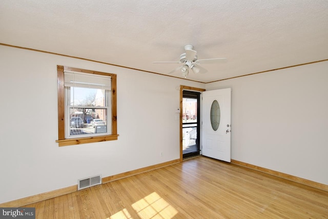 spare room with light wood finished floors, visible vents, ornamental molding, a textured ceiling, and baseboards