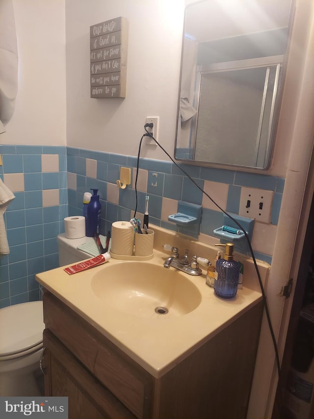 bathroom with wainscoting, toilet, vanity, and tile walls