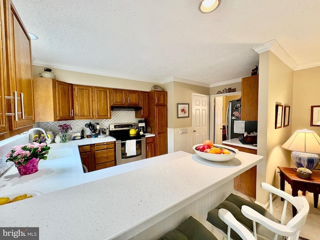 kitchen with light countertops, appliances with stainless steel finishes, brown cabinetry, a sink, and a peninsula