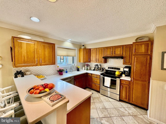 kitchen with brown cabinets, stainless steel appliances, light countertops, a peninsula, and under cabinet range hood