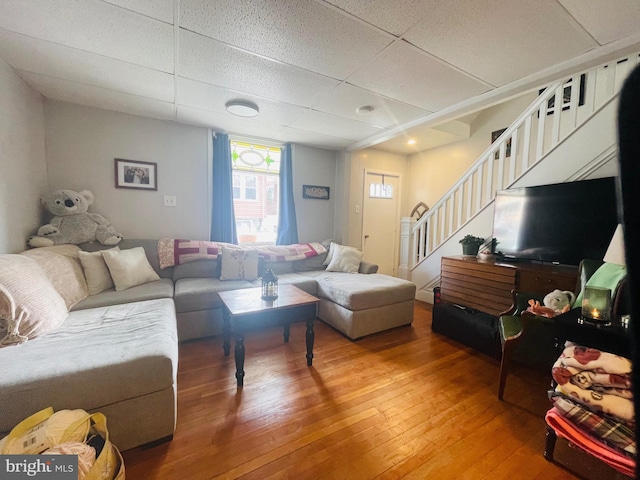 living area with stairs, a paneled ceiling, and light wood-style flooring