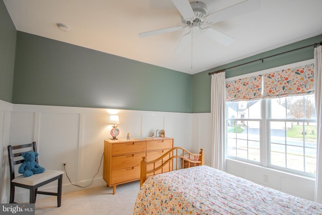 bedroom featuring light carpet, wainscoting, and a decorative wall