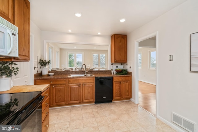 kitchen with brown cabinetry, baseboards, visible vents, a sink, and black appliances