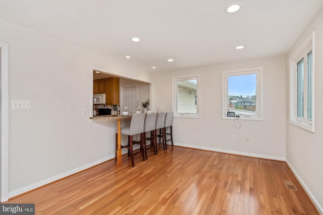 interior space featuring brown cabinets, a breakfast bar area, light wood finished floors, baseboards, and white microwave