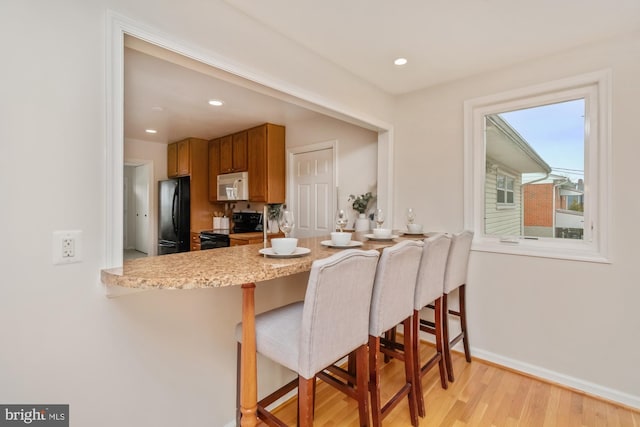 kitchen featuring a kitchen breakfast bar, a peninsula, black appliances, and light wood-style flooring