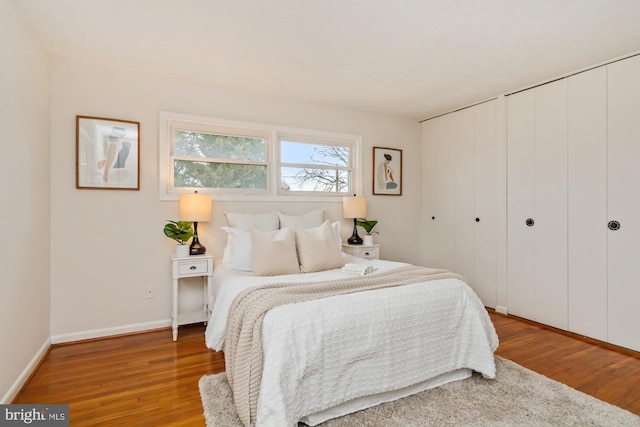 bedroom featuring light wood-style flooring, baseboards, and multiple closets