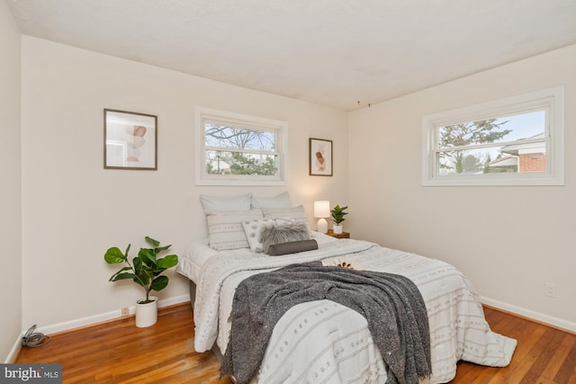 bedroom featuring baseboards, multiple windows, and wood finished floors