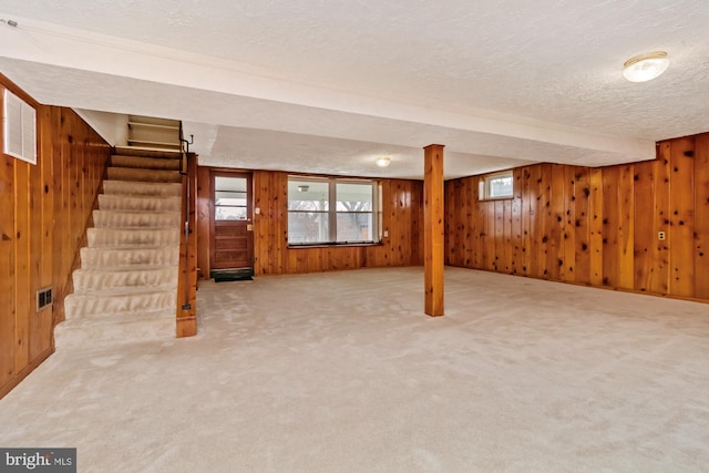 below grade area with visible vents, wood walls, stairs, carpet flooring, and a textured ceiling