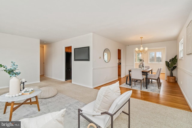 living area with light carpet, a notable chandelier, light wood-style flooring, and baseboards