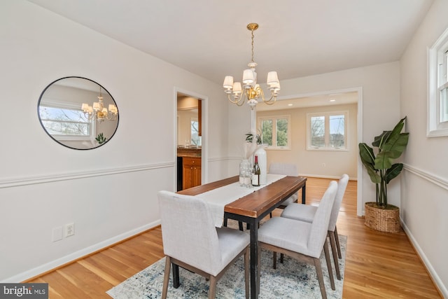 dining area with baseboards, light wood-style floors, a healthy amount of sunlight, and a chandelier