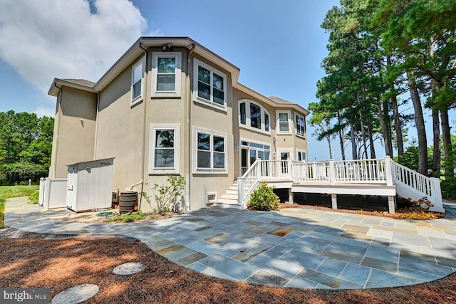 rear view of house featuring a deck, a patio, cooling unit, and stucco siding