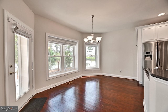 unfurnished dining area featuring dark wood-style flooring, a notable chandelier, recessed lighting, visible vents, and baseboards