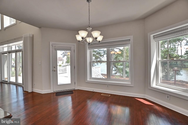 unfurnished dining area featuring hardwood / wood-style flooring, plenty of natural light, visible vents, and a notable chandelier