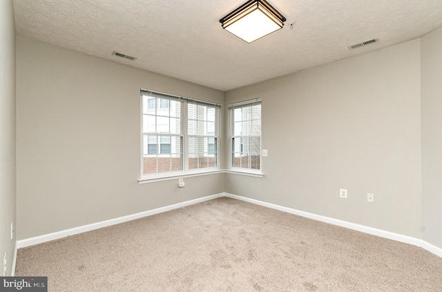 carpeted empty room with a textured ceiling, visible vents, and baseboards